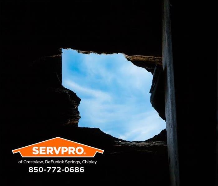 Clouds and blue sky are visible through a hole in a roof.
